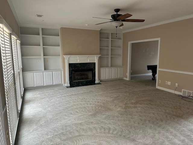 unfurnished living room featuring ceiling fan, a high end fireplace, ornamental molding, light carpet, and built in shelves