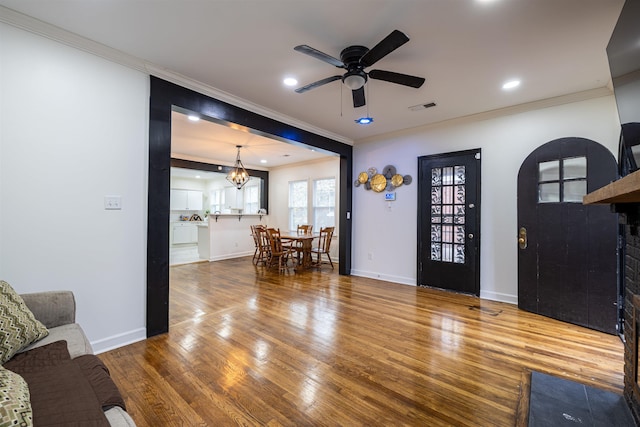 living room featuring hardwood / wood-style floors, ceiling fan with notable chandelier, and ornamental molding