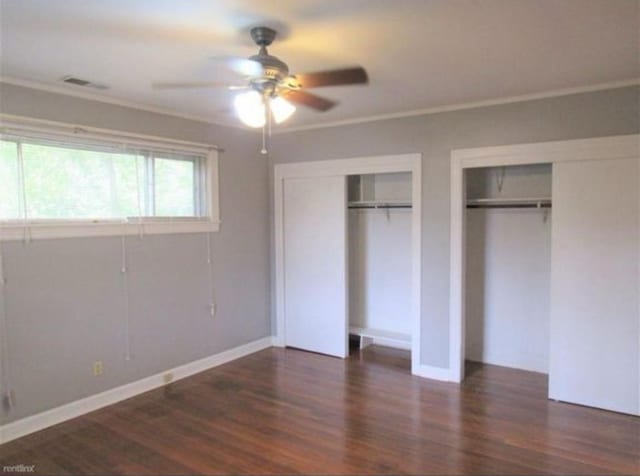 unfurnished bedroom with ornamental molding, two closets, ceiling fan, and dark hardwood / wood-style floors