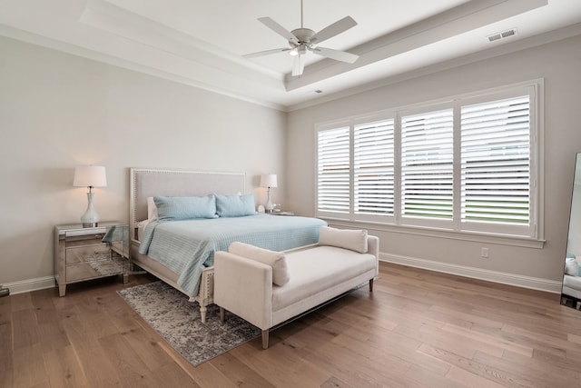 bedroom with hardwood / wood-style flooring, a raised ceiling, and multiple windows