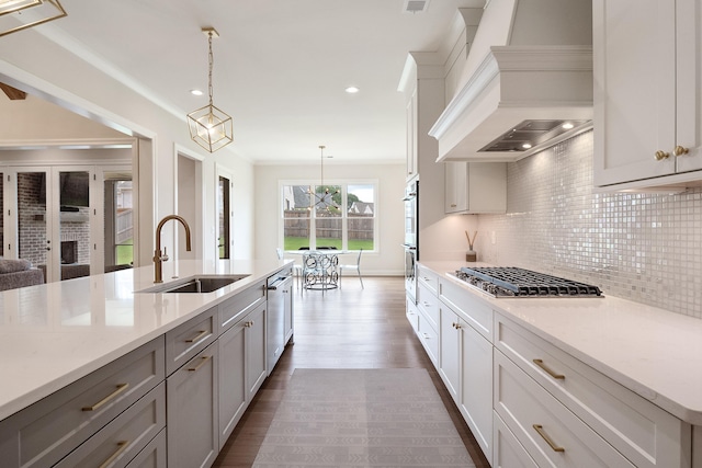 kitchen featuring appliances with stainless steel finishes, hardwood / wood-style floors, sink, pendant lighting, and custom range hood