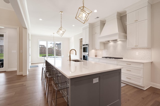 kitchen featuring hardwood / wood-style floors, premium range hood, hanging light fixtures, and a large island with sink