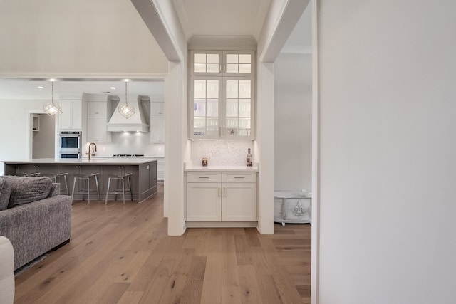 bar featuring white cabinetry, premium range hood, light hardwood / wood-style floors, and decorative light fixtures