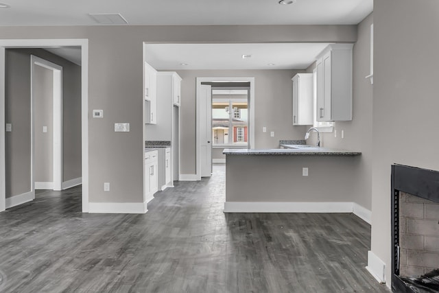 kitchen with white cabinetry, kitchen peninsula, dark hardwood / wood-style flooring, and dark stone counters