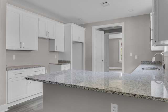 kitchen featuring light stone counters, white cabinetry, kitchen peninsula, and sink