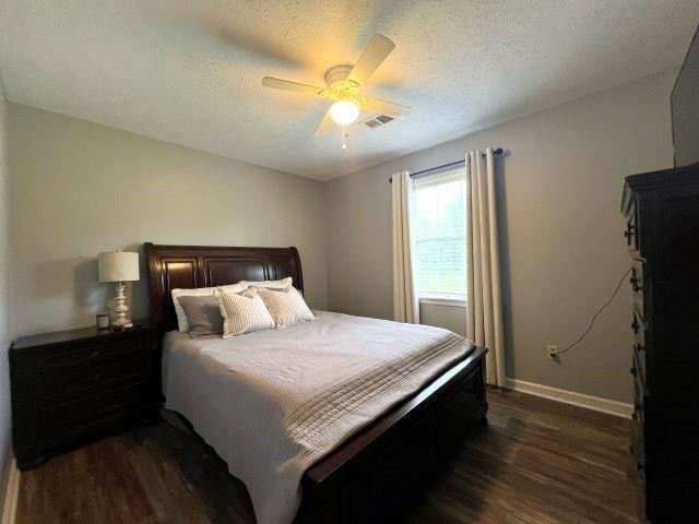 bedroom with a textured ceiling, ceiling fan, and dark hardwood / wood-style floors