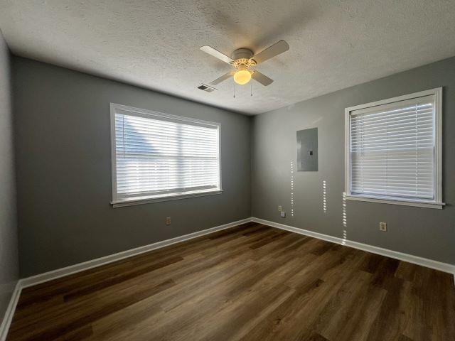 spare room featuring ceiling fan, dark hardwood / wood-style flooring, a textured ceiling, and electric panel