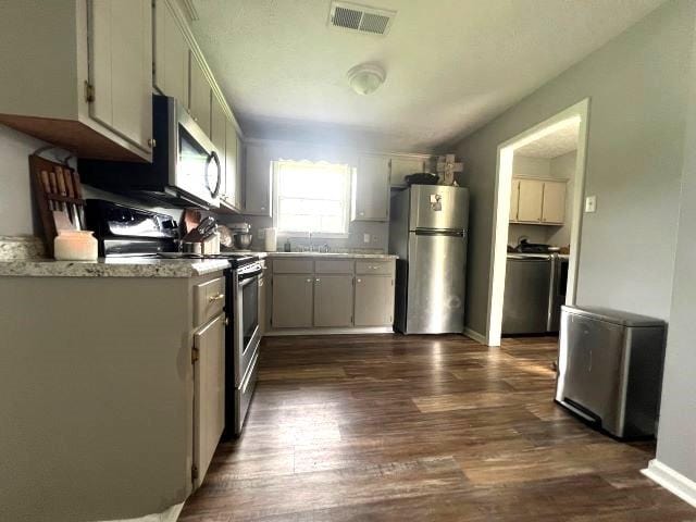 kitchen featuring sink, dark hardwood / wood-style floors, light stone counters, washer / dryer, and stainless steel appliances