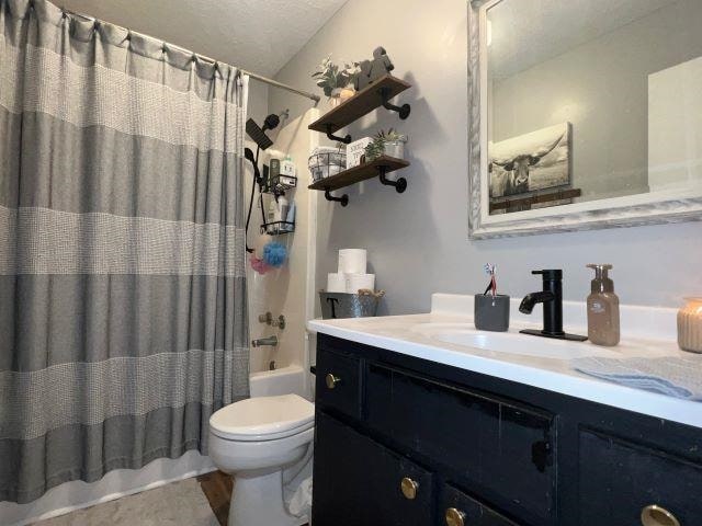 full bathroom featuring vanity, toilet, shower / bathtub combination with curtain, and a textured ceiling