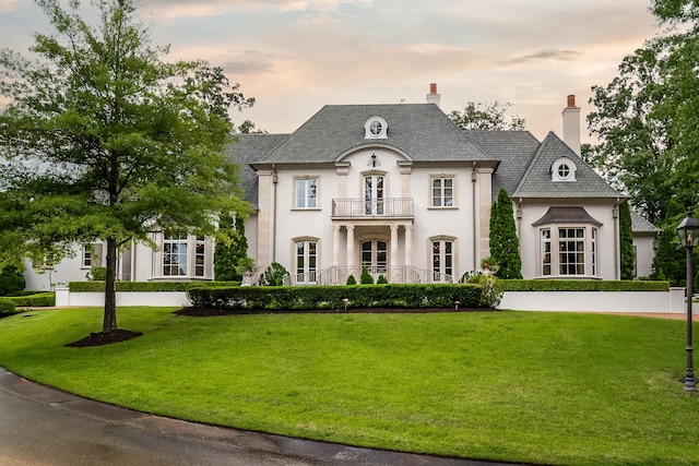 french country home featuring a balcony and a lawn