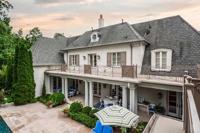 back house at dusk featuring a balcony and a patio