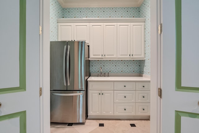 kitchen with sink, white cabinets, stainless steel fridge, ornamental molding, and light tile patterned floors