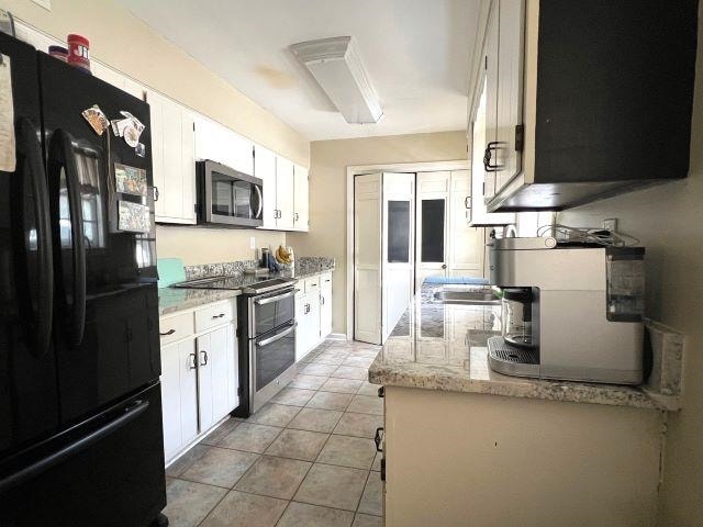 kitchen with appliances with stainless steel finishes, white cabinets, light stone countertops, light tile patterned floors, and sink