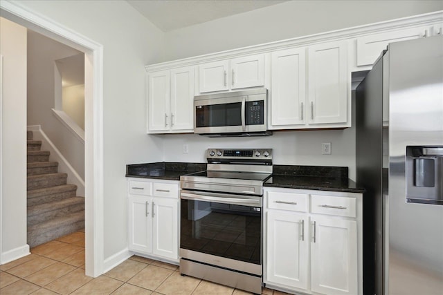 kitchen with stainless steel appliances, dark stone counters, white cabinets, and light tile patterned flooring