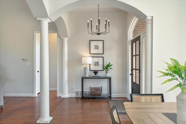 foyer with dark wood-type flooring, decorative columns, and a notable chandelier