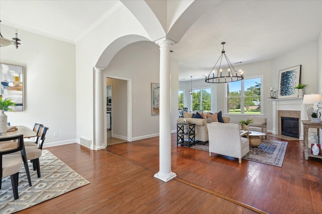 living room with ornate columns, an inviting chandelier, ornamental molding, dark hardwood / wood-style floors, and a tile fireplace