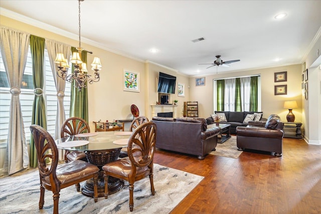 dining space featuring ceiling fan with notable chandelier, wood-type flooring, and ornamental molding