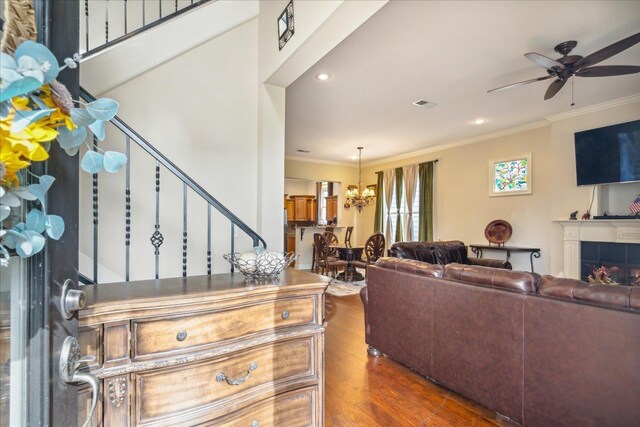 living room with a tile fireplace, hardwood / wood-style flooring, ceiling fan with notable chandelier, and crown molding