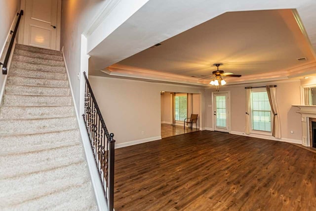 unfurnished living room with dark wood-type flooring, ceiling fan, a tray ceiling, and crown molding