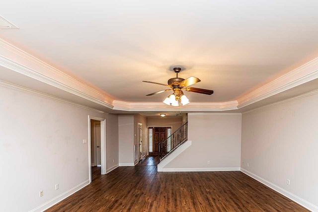 empty room with crown molding, dark wood-type flooring, ceiling fan, and a tray ceiling