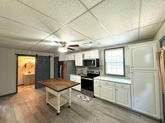 kitchen featuring a paneled ceiling, stainless steel appliances, decorative backsplash, light wood-type flooring, and white cabinetry