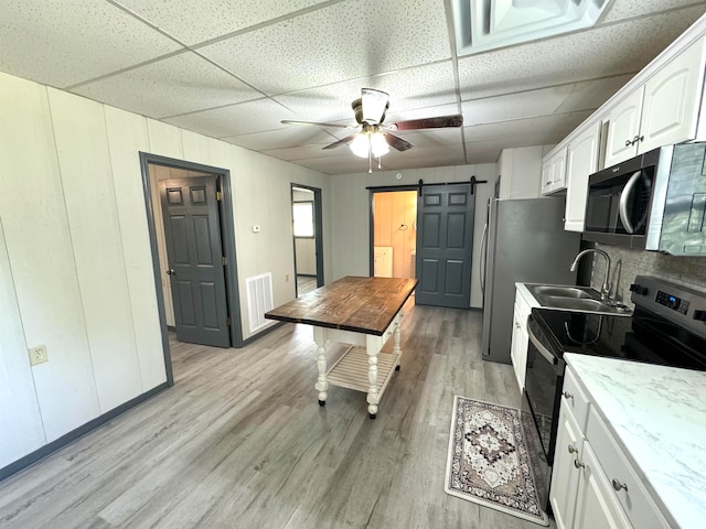 kitchen featuring appliances with stainless steel finishes, light hardwood / wood-style flooring, white cabinets, and a paneled ceiling