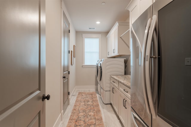 laundry room with washing machine and clothes dryer, light wood-type flooring, and cabinets