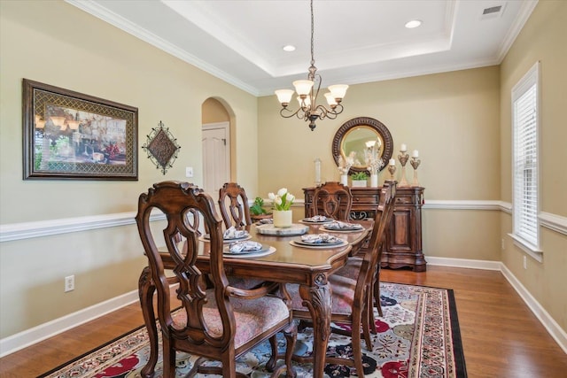 dining area with a chandelier, ornamental molding, a raised ceiling, and hardwood / wood-style floors