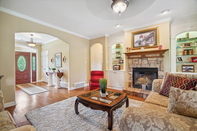 living room featuring crown molding, a fireplace, built in shelves, and wood-type flooring