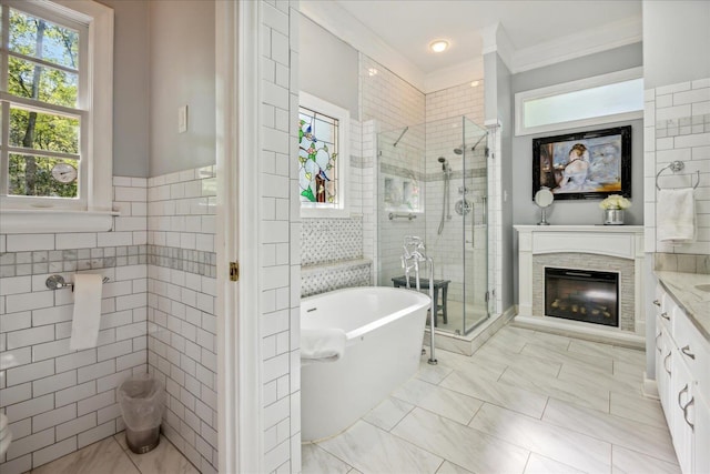 full bathroom with a freestanding tub, vanity, tile walls, a stall shower, and a glass covered fireplace