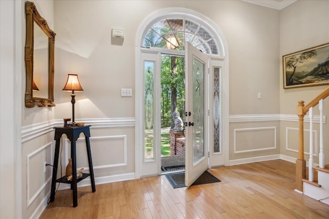 foyer with light wood-style flooring, stairs, a decorative wall, and wainscoting