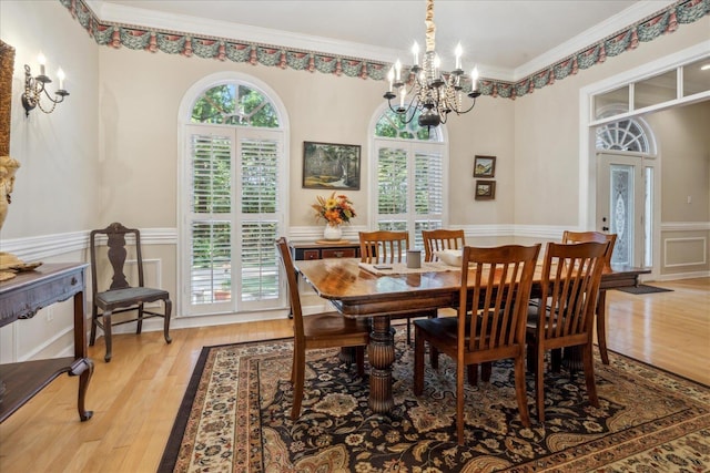 dining room with ornamental molding, light wood-type flooring, wainscoting, and a decorative wall