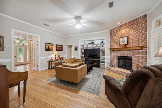 living area with visible vents, a textured ceiling, crown molding, light wood-type flooring, and a fireplace