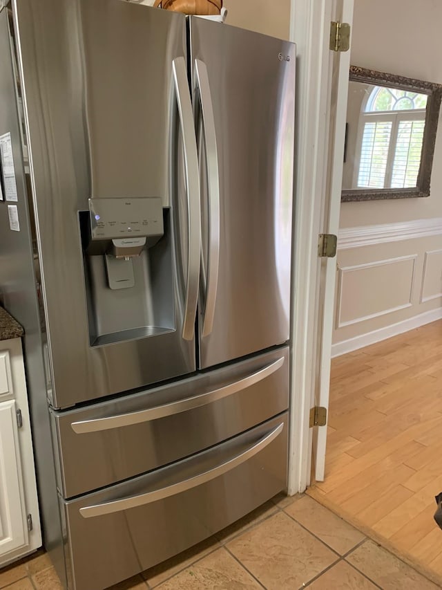 details featuring light wood finished floors, stainless steel fridge, wainscoting, white cabinetry, and a decorative wall