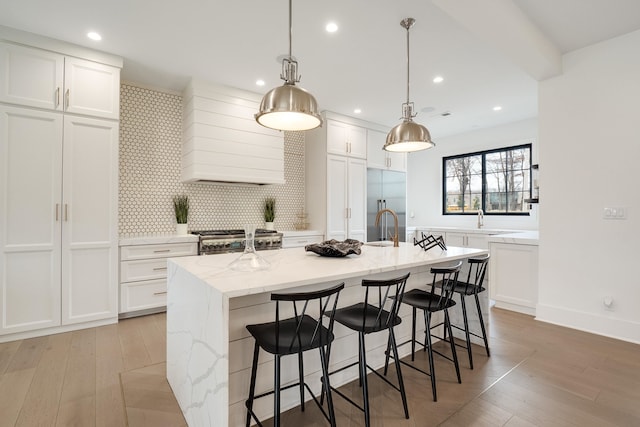 kitchen featuring hanging light fixtures, premium range hood, white cabinets, and a center island with sink