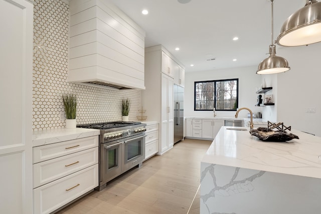 kitchen with white cabinets, light hardwood / wood-style floors, decorative backsplash, high quality appliances, and sink