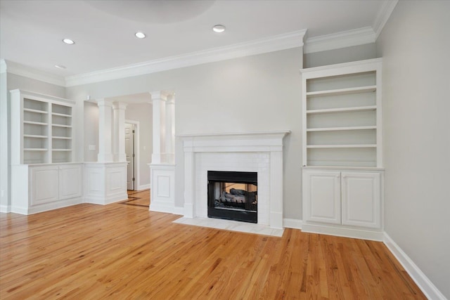 unfurnished living room with ornate columns, a fireplace, built in shelves, and light wood-type flooring