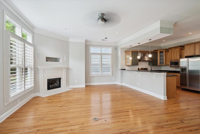 kitchen with pendant lighting, appliances with stainless steel finishes, a kitchen breakfast bar, kitchen peninsula, and wall chimney exhaust hood