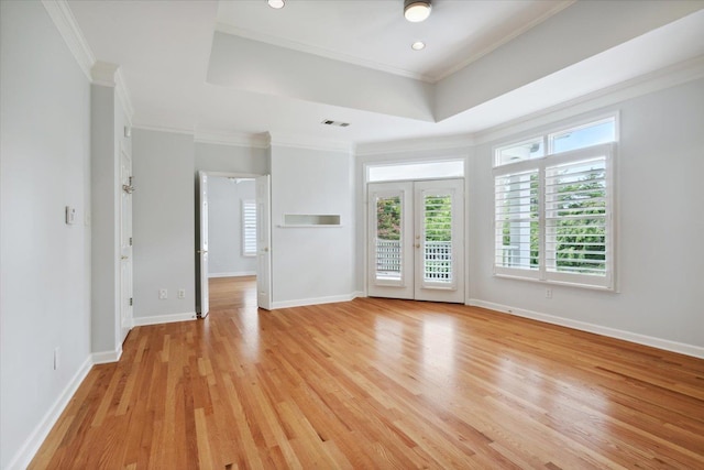 empty room featuring crown molding, light hardwood / wood-style flooring, a raised ceiling, and french doors