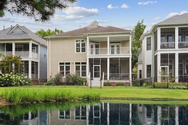 back of house featuring a balcony, a water view, and a lawn