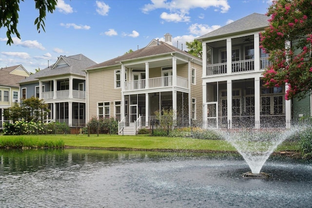 rear view of house with a water view, a sunroom, and a lawn