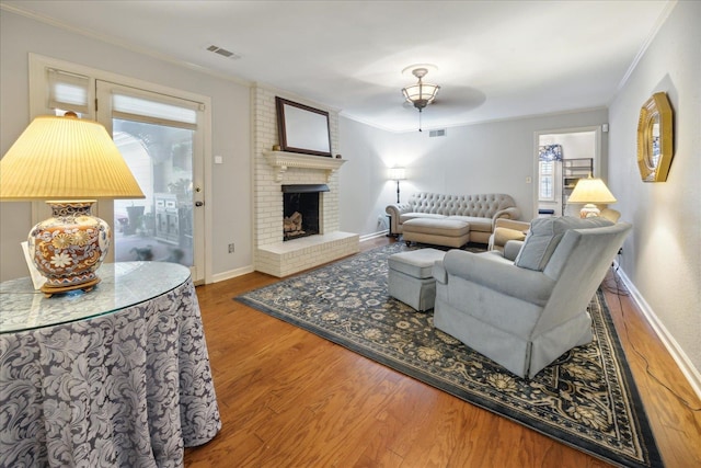 living room with brick wall, crown molding, a brick fireplace, and hardwood / wood-style flooring