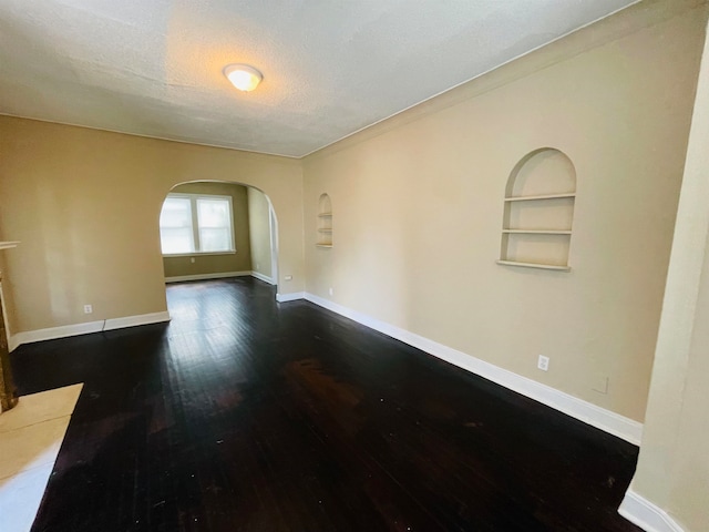 empty room featuring dark hardwood / wood-style flooring, built in features, and a textured ceiling