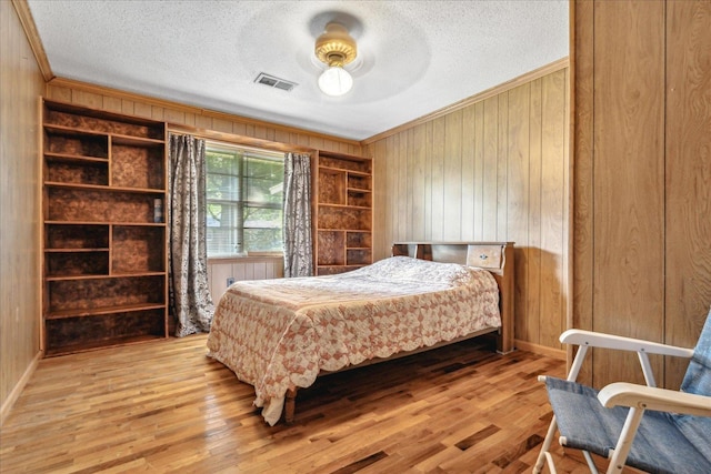 bedroom featuring wood walls, ornamental molding, a textured ceiling, and light hardwood / wood-style flooring