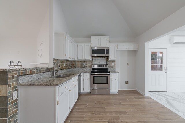 kitchen featuring stainless steel appliances, vaulted ceiling, sink, light stone counters, and a wall mounted air conditioner