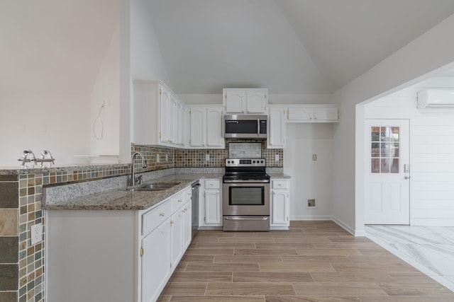 kitchen with appliances with stainless steel finishes, sink, stone countertops, a wall unit AC, and white cabinets