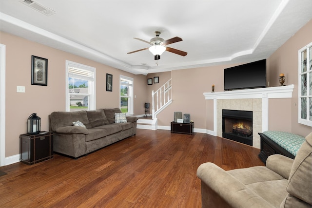 living room with a raised ceiling, a tile fireplace, ceiling fan, and hardwood / wood-style floors