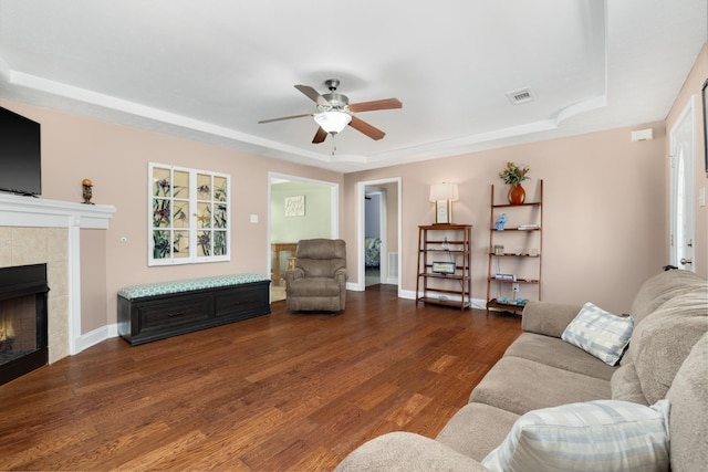 living room with ceiling fan, hardwood / wood-style flooring, a tiled fireplace, and a raised ceiling