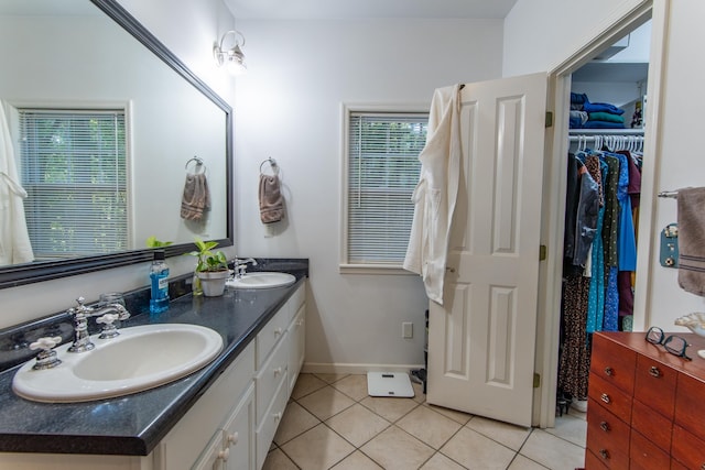 full bath featuring double vanity, a spacious closet, a sink, tile patterned flooring, and baseboards