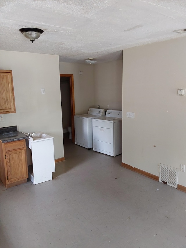 laundry room featuring washing machine and clothes dryer, cabinets, and a textured ceiling